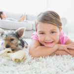 child and puppy laying on clean white carpet